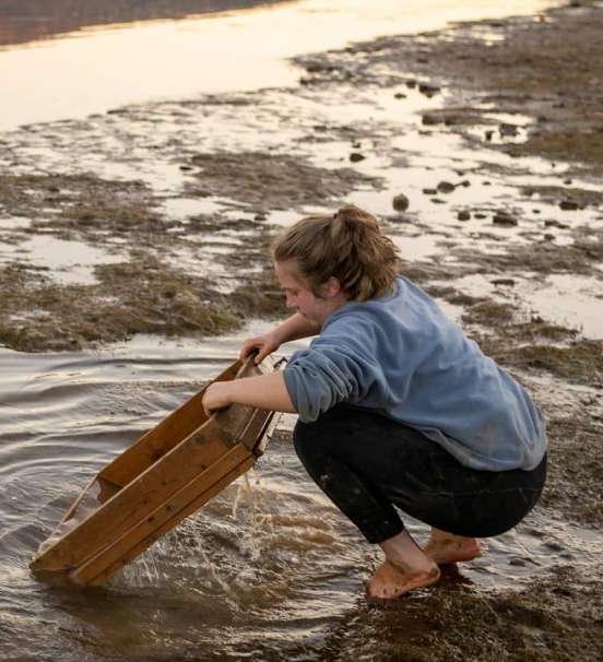 Student sifting soil in shallow river