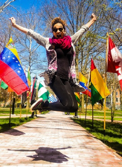 International Week participant jumping in front of a row of international flags.